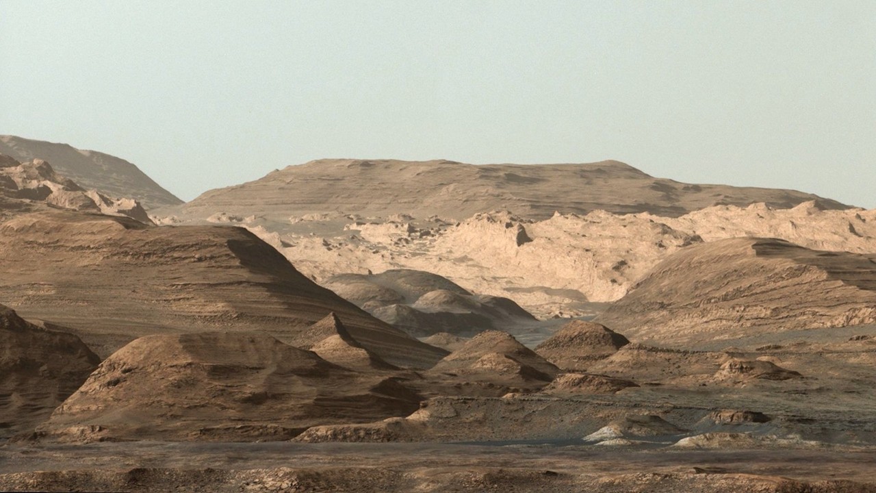 a dusty regolith plain with scattered rocks, a linear track imprint, and a sharp triangular shadow